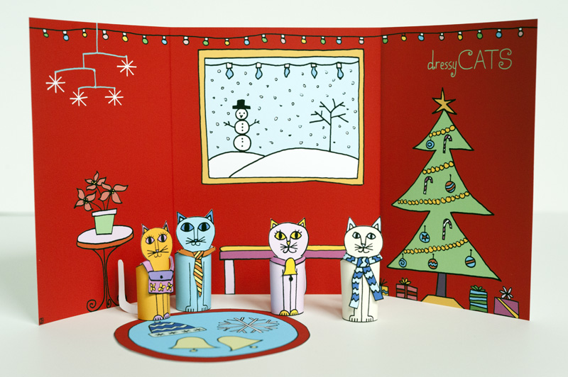 Una familia gato en cartulina cuyo fondo es el dibujo de un salón en navidad